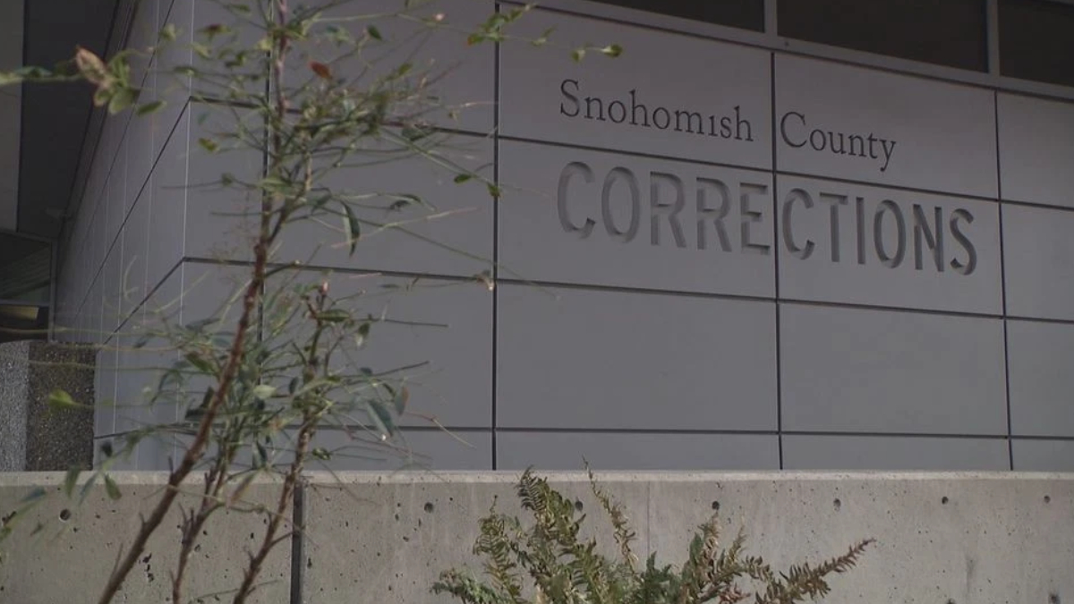 Exterior view of Snohomish County Corrections building with large raised lettering on gray panels and some plants in the foreground.