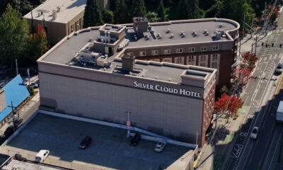 Aerial view of the Silver Cloud Hotel showing a large brick building with a sign reading 'Silver Cloud Hotel' and a mostly empty parking lot on the foreground.