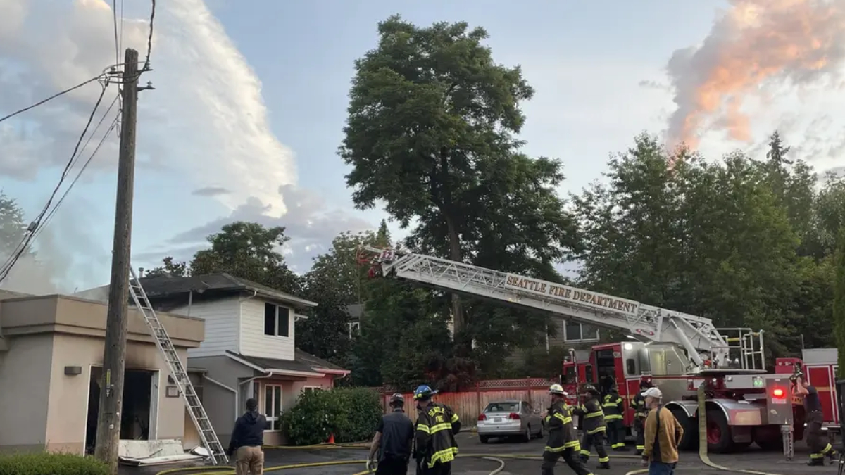Seattle Fire Department uses an aerial ladder to reach a two-story house as firefighters work on a residential street.
