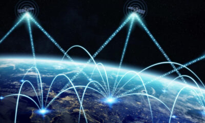 Global communications network: satellites in space transmitting bright data beams to multiple ground stations over Earth at night.