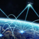 Global communications network: satellites in space transmitting bright data beams to multiple ground stations over Earth at night.