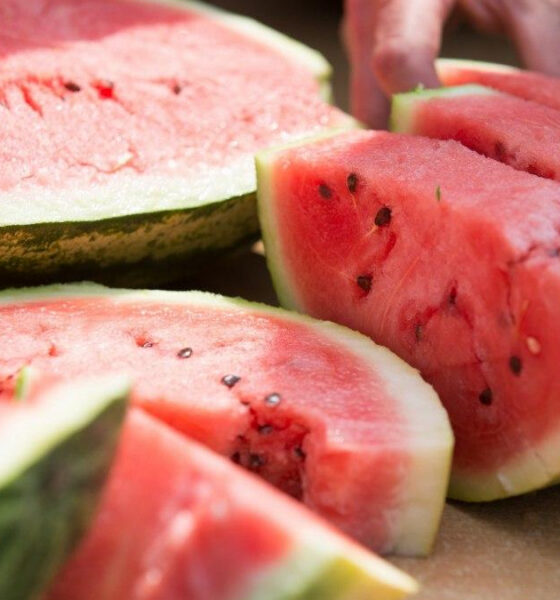 Sliced ripe watermelon on a cutting board, showing pink flesh and black seeds in the fruit's interior.