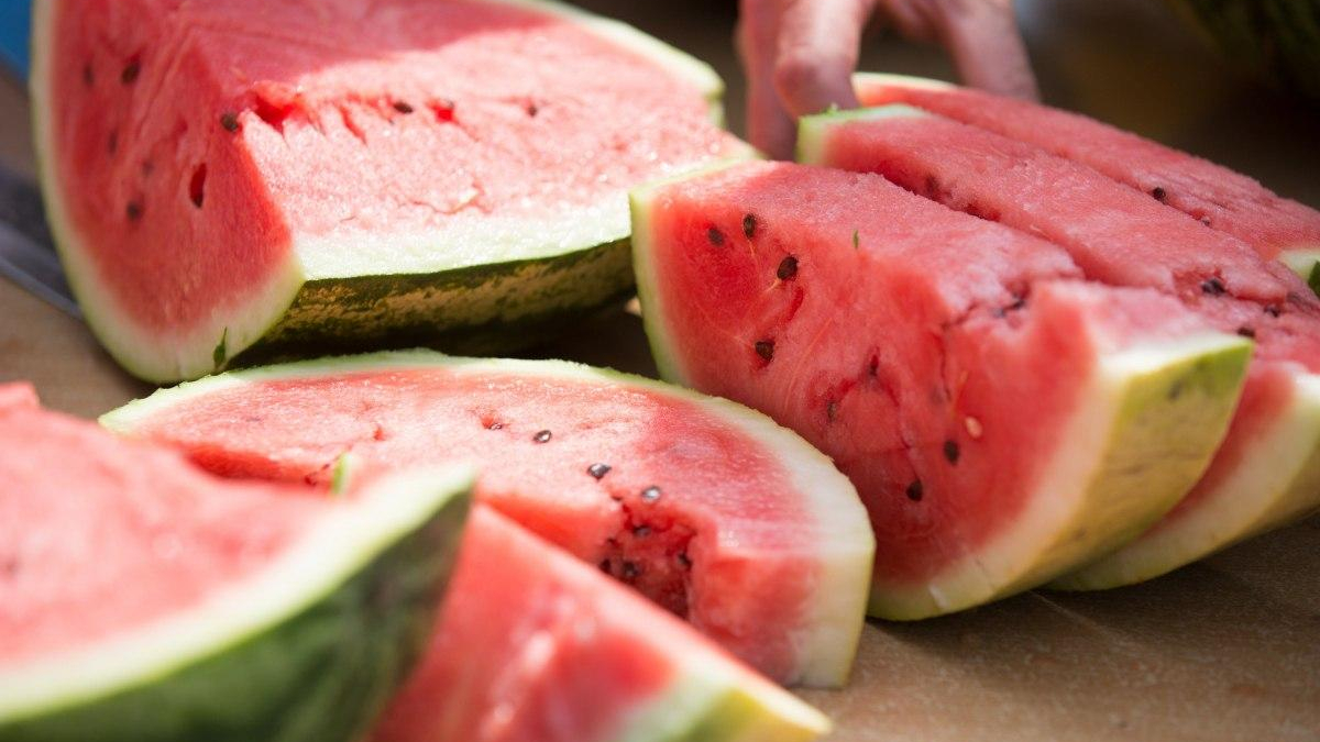 Sliced ripe watermelon on a cutting board, showing pink flesh and black seeds in the fruit's interior.