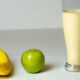 Bananas, a green apple, and a tall glass of creamy banana smoothie on a white surface.