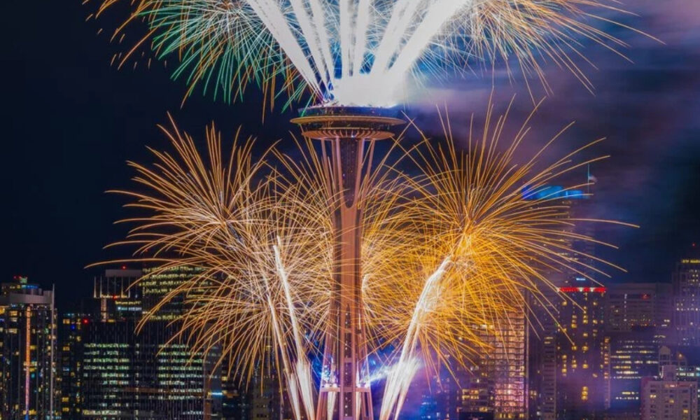 Fireworks explode around the Space Needle against a nighttime Seattle skyline.