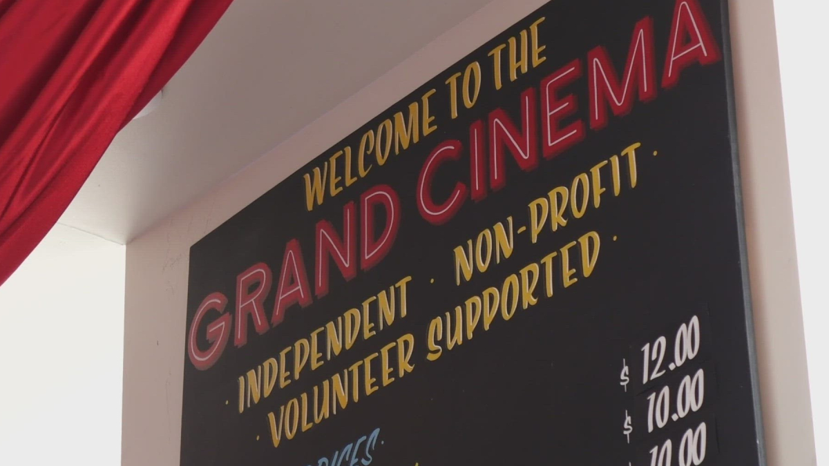 Chalkboard-style sign saying 'Welcome to the Grand Cinema' with yellow list items: Independent, Non-Profit, Volunteer Supported, visible red-outline 'GRAND CINEMA' text.