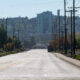 Empty urban street lined with utility poles and trees, stretching toward distant buildings and a clear blue sky.