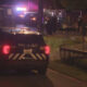 Nighttime scene with a Seattle Police SUV and flashing emergency lights parked on a street near a fenced area, with officers in the background.