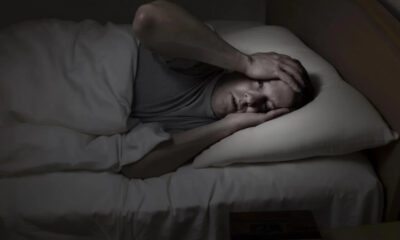 Man lying in bed at night, clutching his head with both hands in apparent headache or distress.