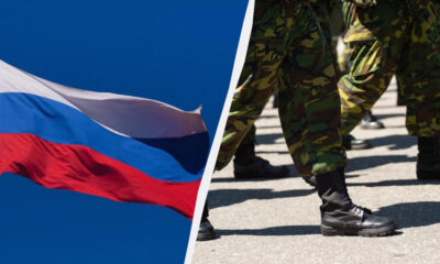 Russian flag waving beside soldiers marching in formation on a paved surface.