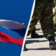Russian flag waving beside soldiers marching in formation on a paved surface.