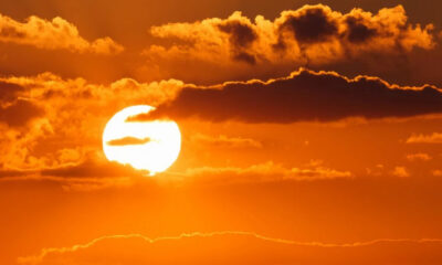 Sun setting over an orange sky with scattered clouds and a bright sun near the horizon.
