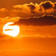 Sun setting over an orange sky with scattered clouds and a bright sun near the horizon.