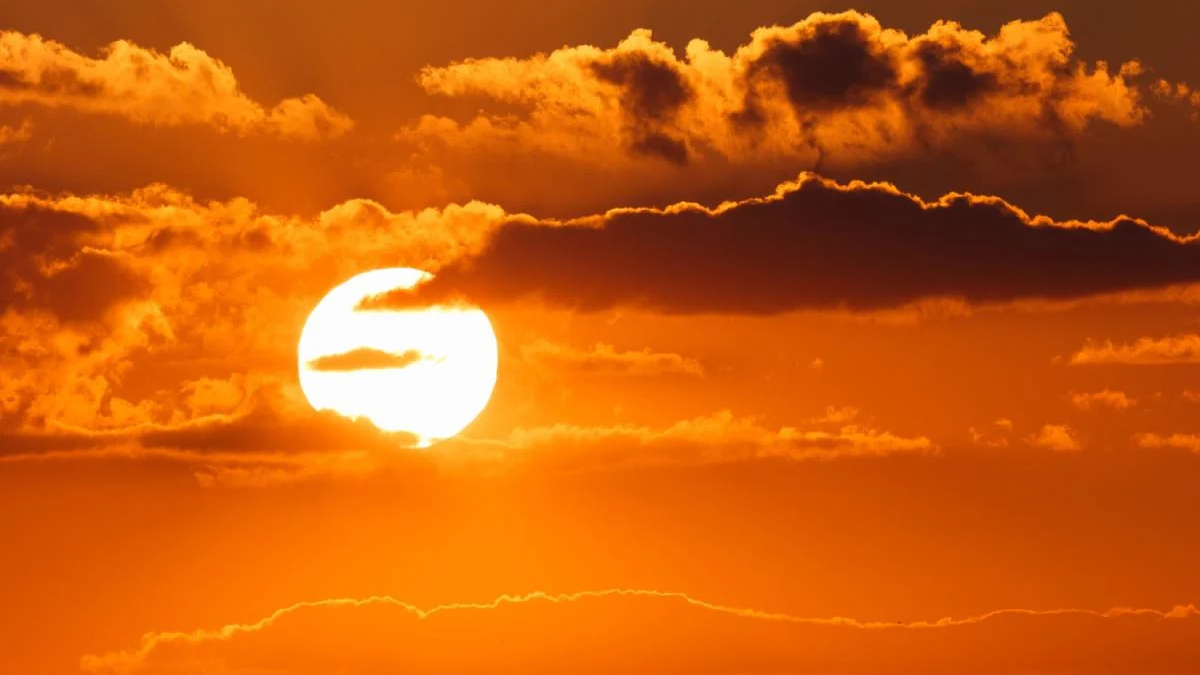 Sun setting over an orange sky with scattered clouds and a bright sun near the horizon.