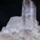 Clear quartz crystal standing upright on a bed of smaller crystals against a black background.