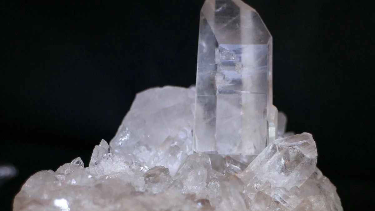 Clear quartz crystal standing upright on a bed of smaller crystals against a black background.