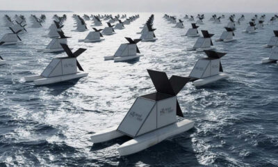 Row of identical white boat sculptures with black sails floating on the sea, arranged in a grid.
