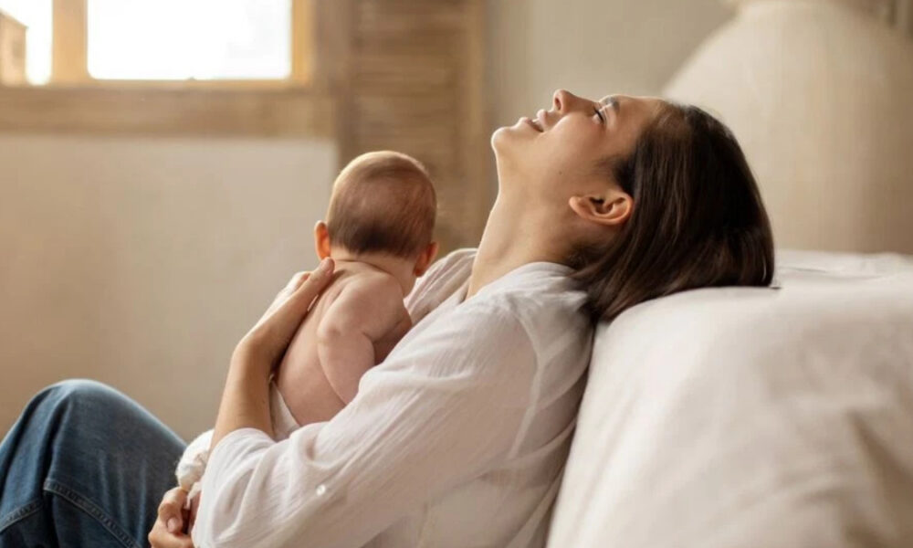 Mother reclining on a sofa, breastfeeding her baby in a calm, sunlit room.