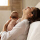 Mother reclining on a sofa, breastfeeding her baby in a calm, sunlit room.