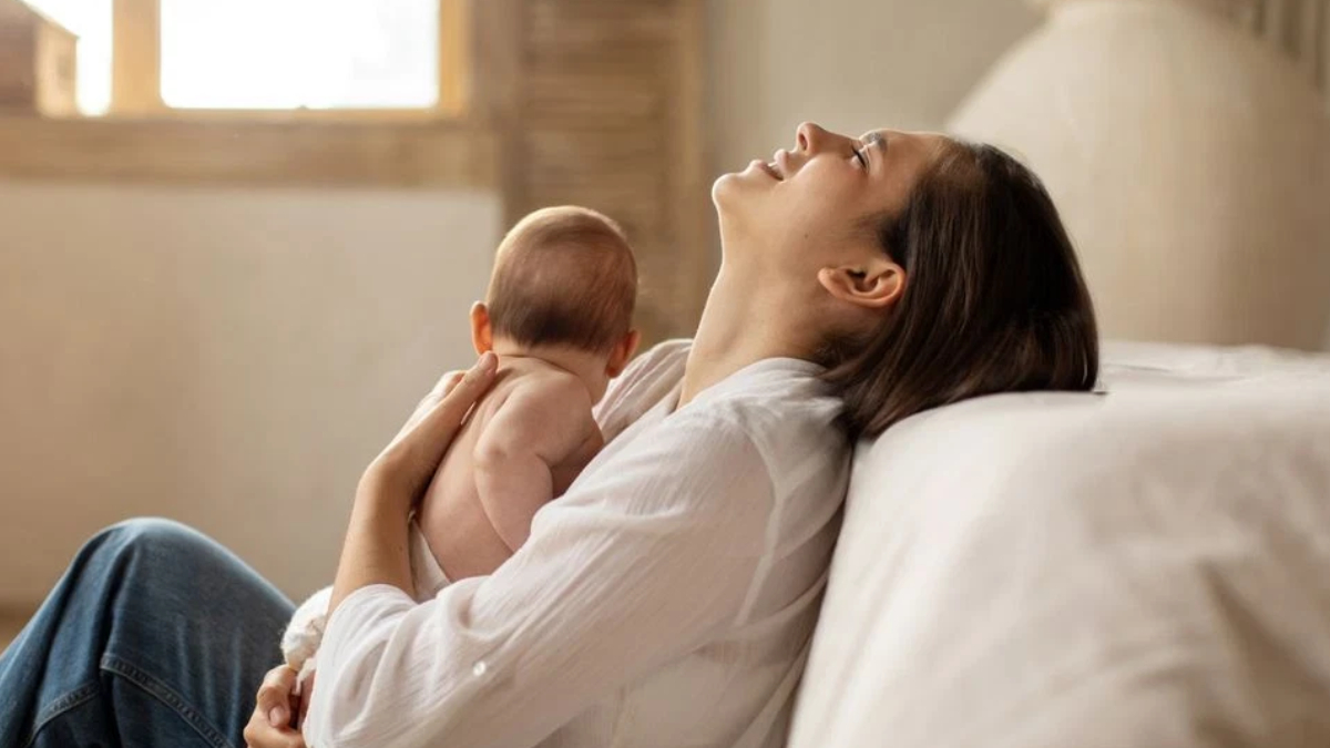 Mother reclining on a sofa, breastfeeding her baby in a calm, sunlit room.