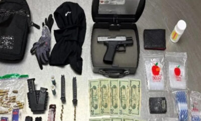 Gun in a hard case with magazines, gloves, and clothing laid out alongside cash and small packets on a gray floor.