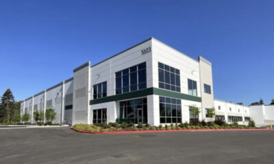 Modern two-story office building with large glass windows, white facade, and landscaped curb; address 5103 visible on the corner.