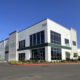 Modern two-story office building with large glass windows, white facade, and landscaped curb; address 5103 visible on the corner.
