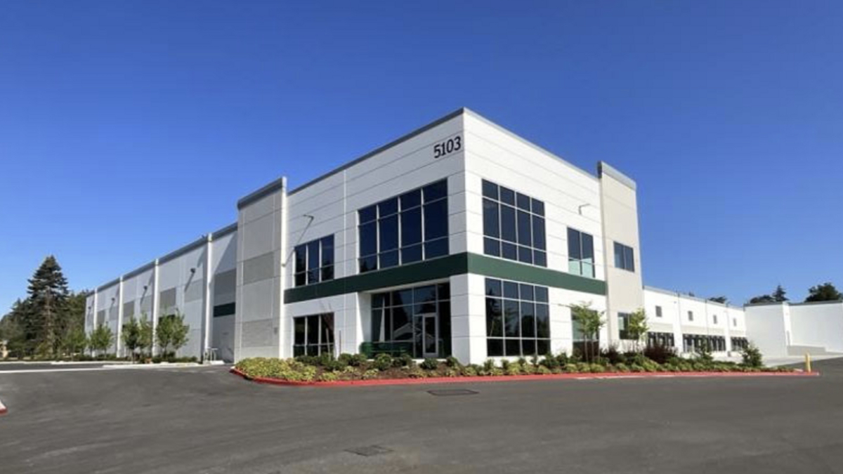 Modern two-story office building with large glass windows, white facade, and landscaped curb; address 5103 visible on the corner.