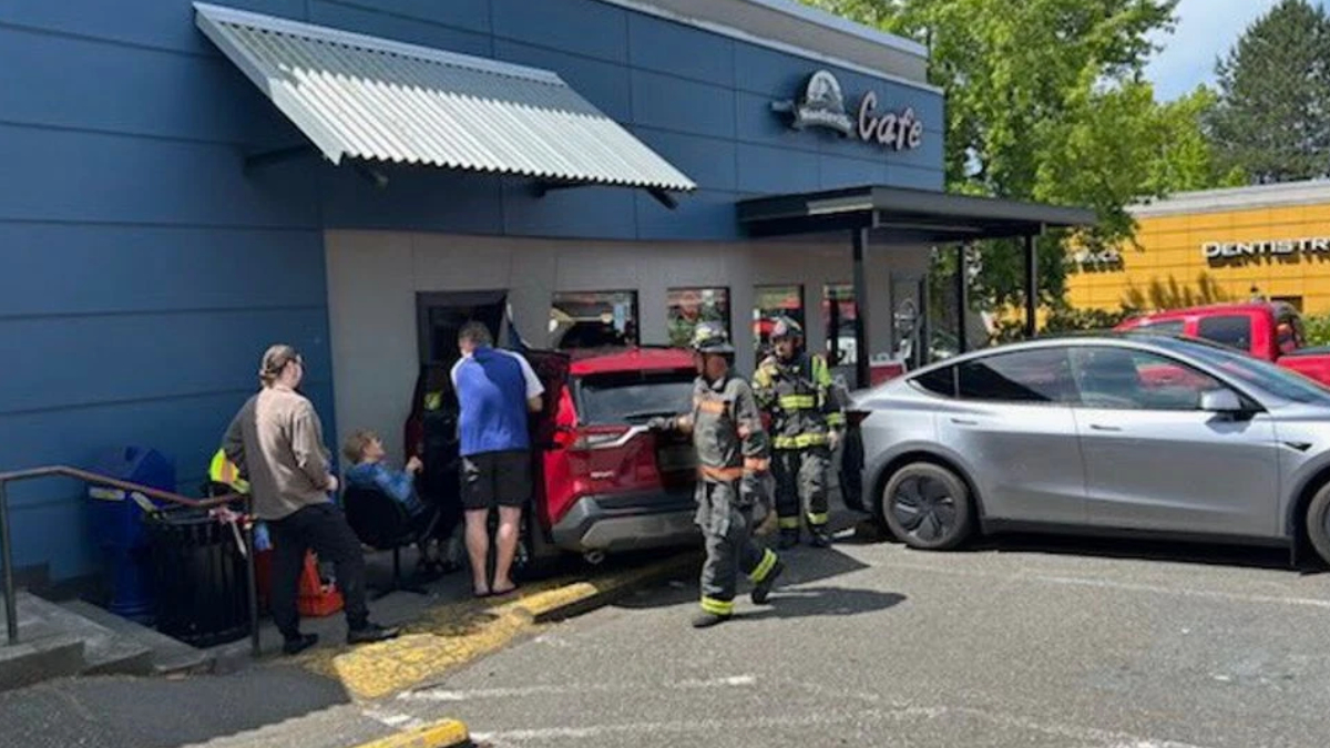 Firefighters and bystanders outside a blue cafe, a red SUV with its trunk open nearby.
