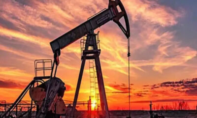 Oil pumpjack silhouetted against a fiery sunset in an open oil field.