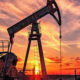 Oil pumpjack silhouetted against a fiery sunset in an open oil field.