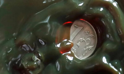 Close-up of a silver coin partially embedded in glossy green slime, with ornate designs visible on the coin.