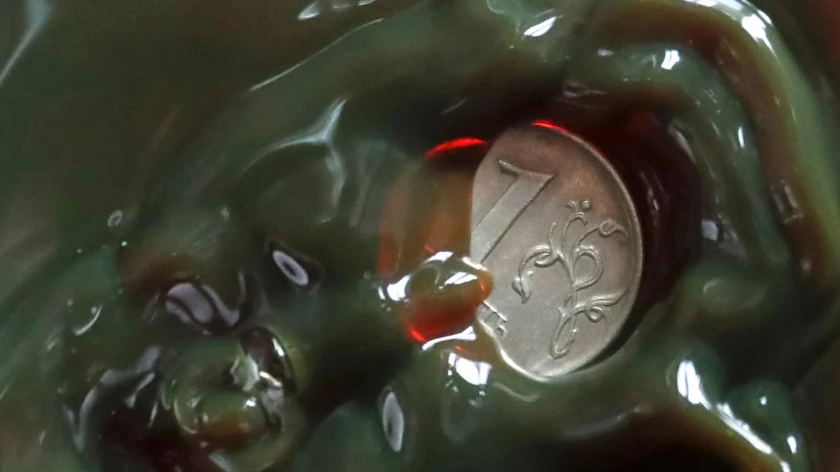 Close-up of a silver coin partially embedded in glossy green slime, with ornate designs visible on the coin.