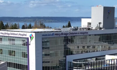 Modern glass-front hospital building with signage reading 'Mary Bridge Children's Hospital' and a distant waterfront.