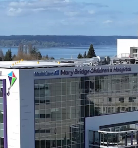 Modern glass-front hospital building with signage reading 'Mary Bridge Children's Hospital' and a distant waterfront.