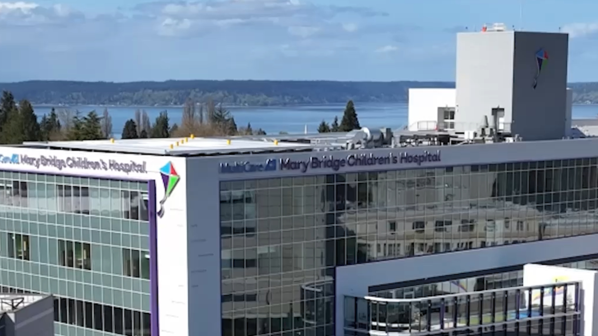 Modern glass-front hospital building with signage reading 'Mary Bridge Children's Hospital' and a distant waterfront.
