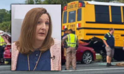 Woman being interviewed in the foreground while a yellow school bus crash with responders is visible in the background.