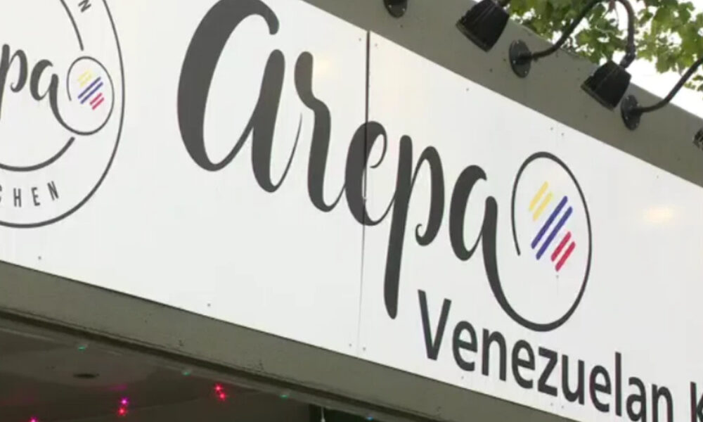 Restaurant sign reading 'Arpa Venezuelan Kitchen' with circular logo and colorful rainbow stripes