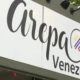Restaurant sign reading 'Arpa Venezuelan Kitchen' with circular logo and colorful rainbow stripes