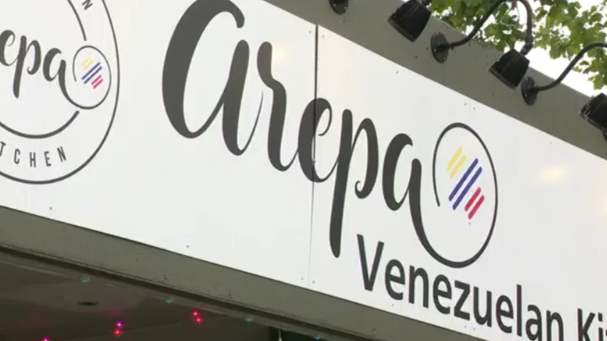 Restaurant sign reading 'Arpa Venezuelan Kitchen' with circular logo and colorful rainbow stripes