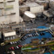 Aerial view of an industrial plant with floodwater surrounding a row of parked cars and large processing equipment nearby to the buildings.