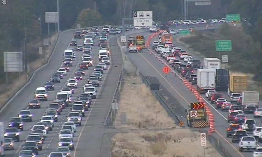 Busy freeway with construction in the center: traffic jam in both directions, orange cones, barriers, and equipment along the median.