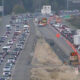 Busy freeway with construction in the center: traffic jam in both directions, orange cones, barriers, and equipment along the median.