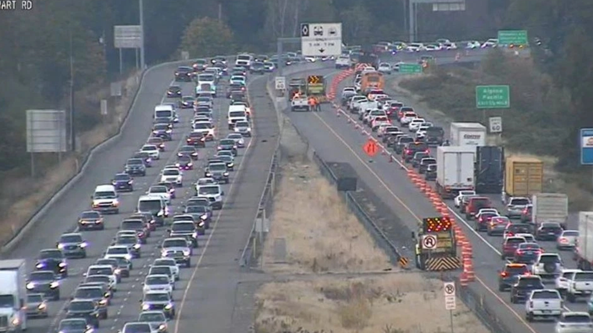 Busy freeway with construction in the center: traffic jam in both directions, orange cones, barriers, and equipment along the median.