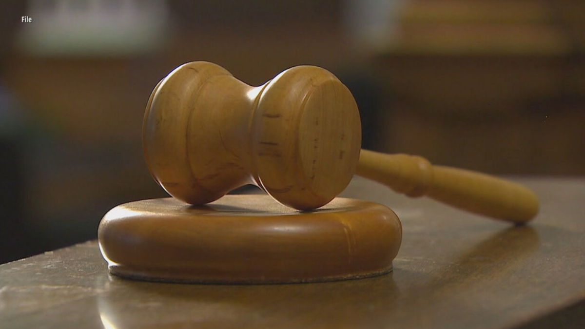 Wooden judge's gavel resting on a round sound block on a wooden table in a courtroom setting.