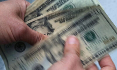 Hands counting a stack of US $100 bills, with Benjamin Franklin's portrait visible on the notes