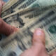 Hands counting a stack of US $100 bills, with Benjamin Franklin's portrait visible on the notes