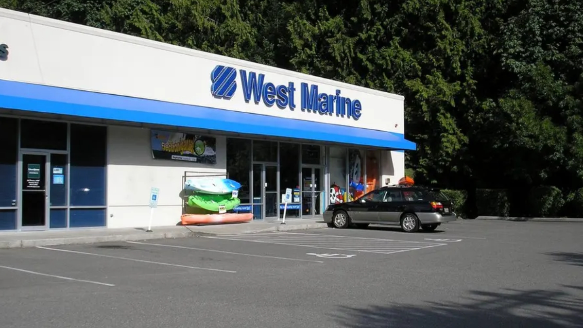 West Marine storefront with stacked kayaks outside and a parked car in the lot.