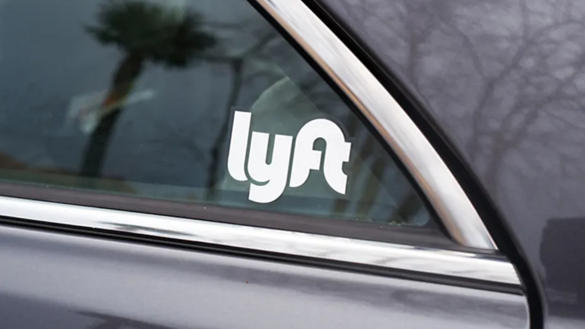Lyft logo sticker on the rear side window of a gray car with chrome trim nearby.