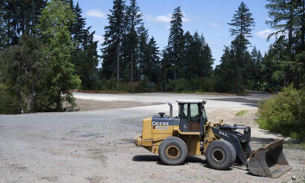 Yellow Deere wheel loader with a large front bucket on a gravel construction site, trees in the background.